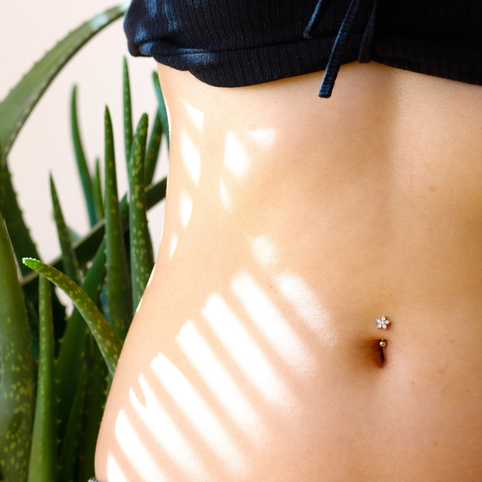 Understated Elegance: Flower Charm Belly Ring with Black Top and Grey Trousers — Belly Button Piercing Ideas