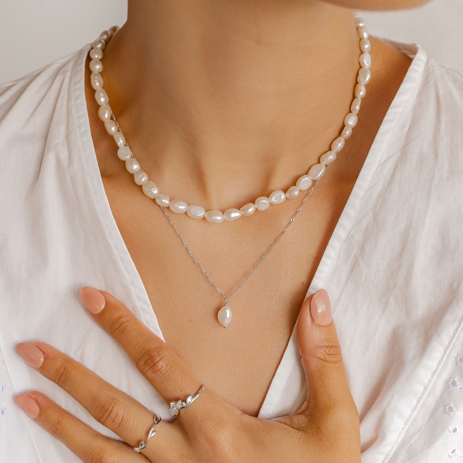Layered Pearl and Silver Chain Necklaces Over White Collared Shirt Layered Pearl and Silver Chain Necklaces Over White Collared Shirt — Pearl Necklace Outfits