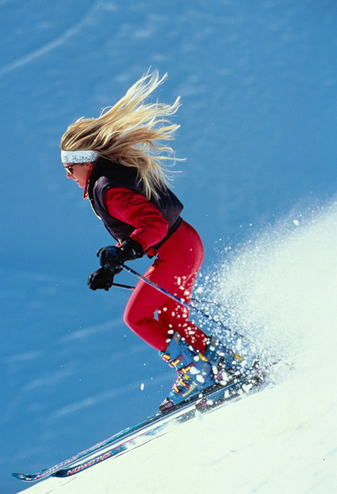 Dynamic Skiing: Red Ski Suit and Black Vest with Blue and White Ski Boots Dynamic Skiing: Red Ski Suit and Black Vest with Blue and White Ski Boots — Salomon Outfits